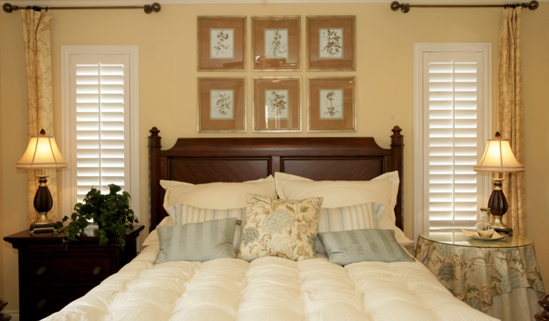 Tall plantation shutters framing bed in a bedroom in Houston 